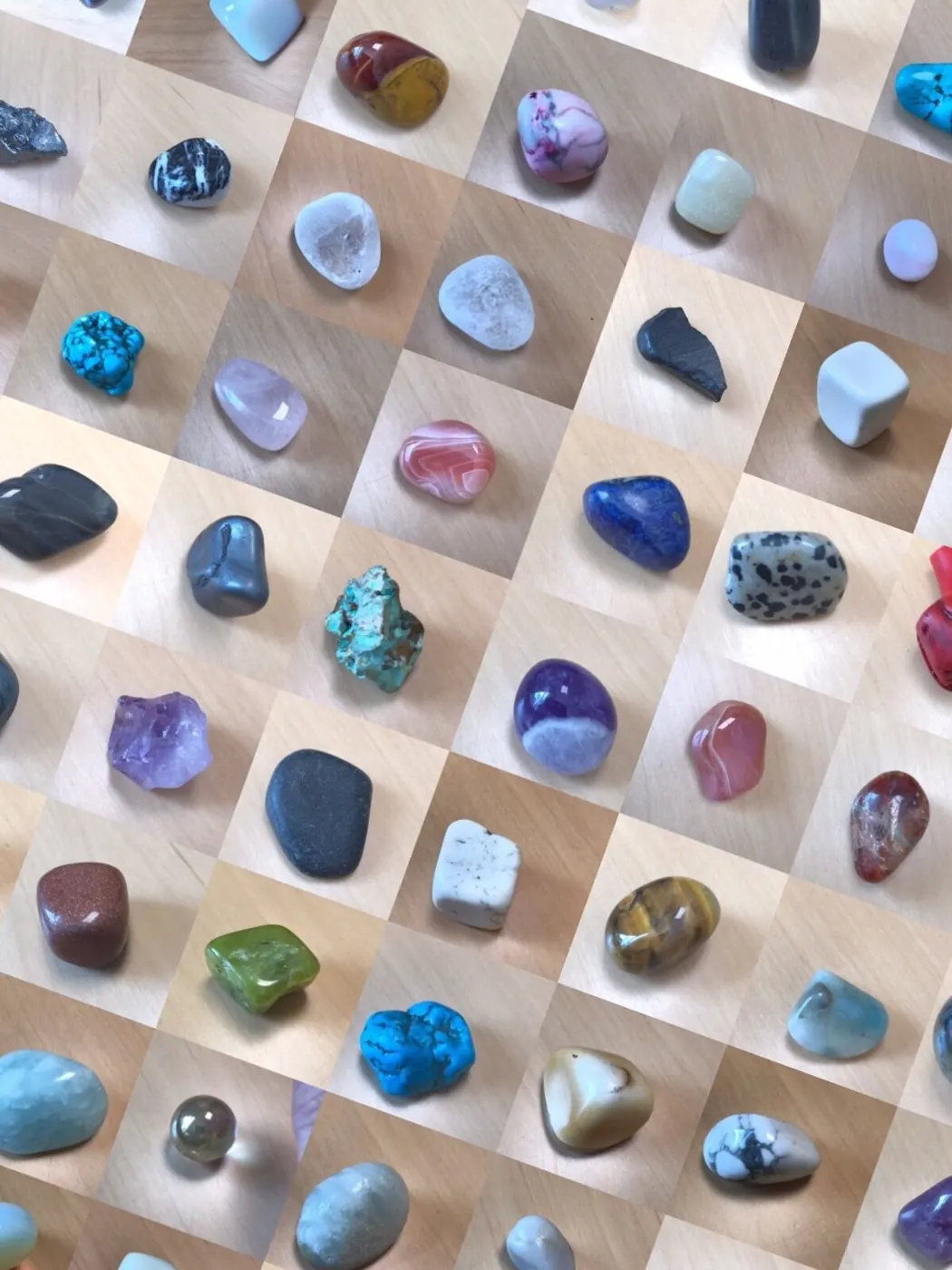 Grid of polished tumbled stones and crystals in many colours laid out on a wooden surface
