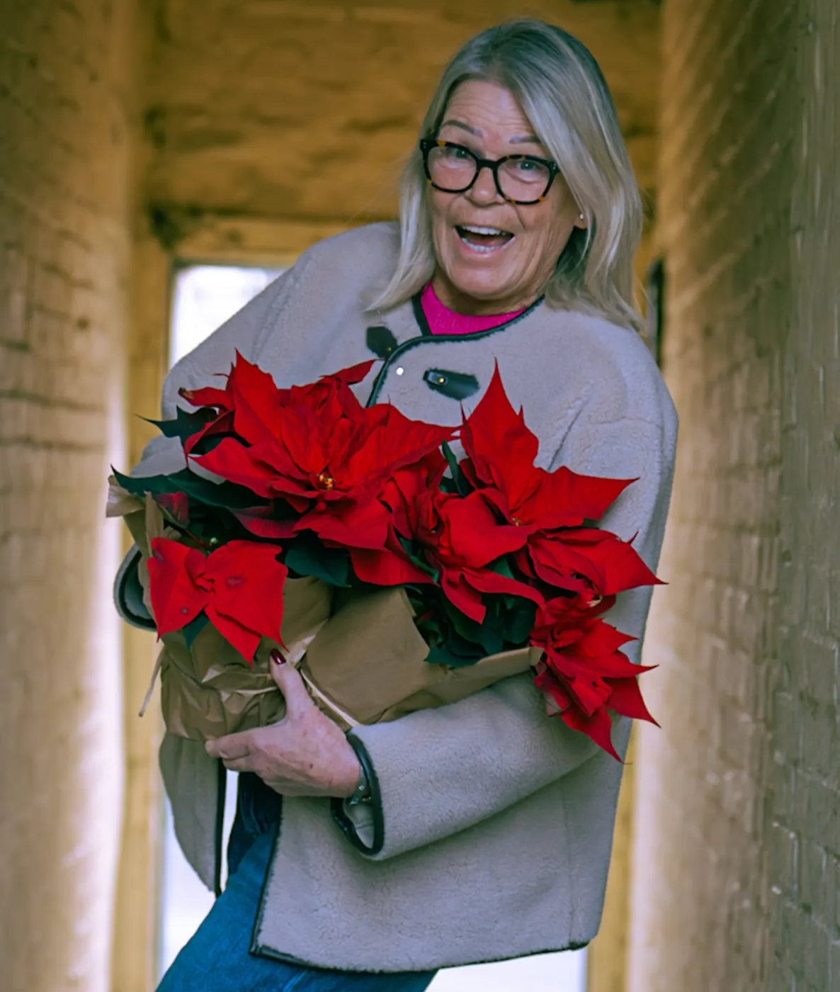 Street portrait of a laughing woman carrying a pot of red poinsettias through a narrow brick passage
