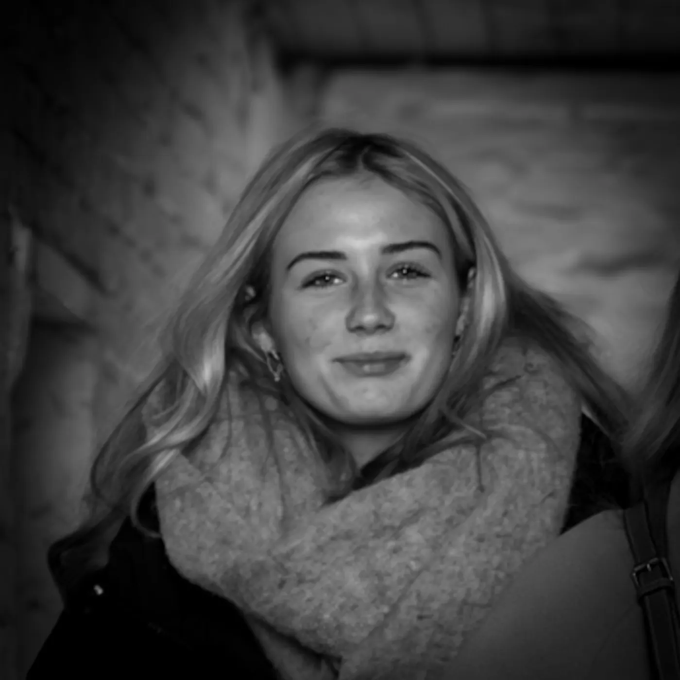 Black and white street portrait of a smiling young woman with long hair and a chunky scarf