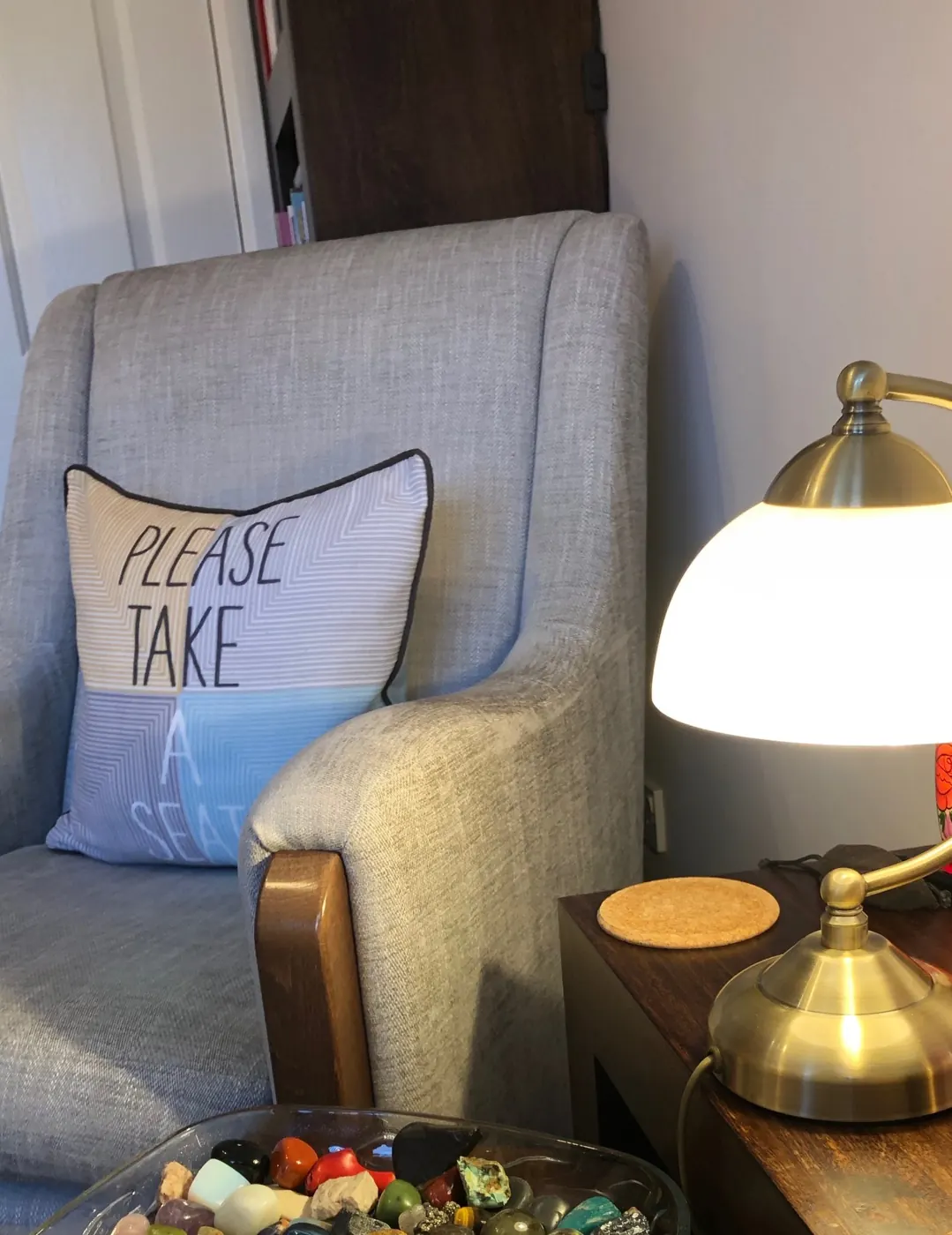 Grey armchair with a Please Take a Seat cushion beside a lamp in a therapy room